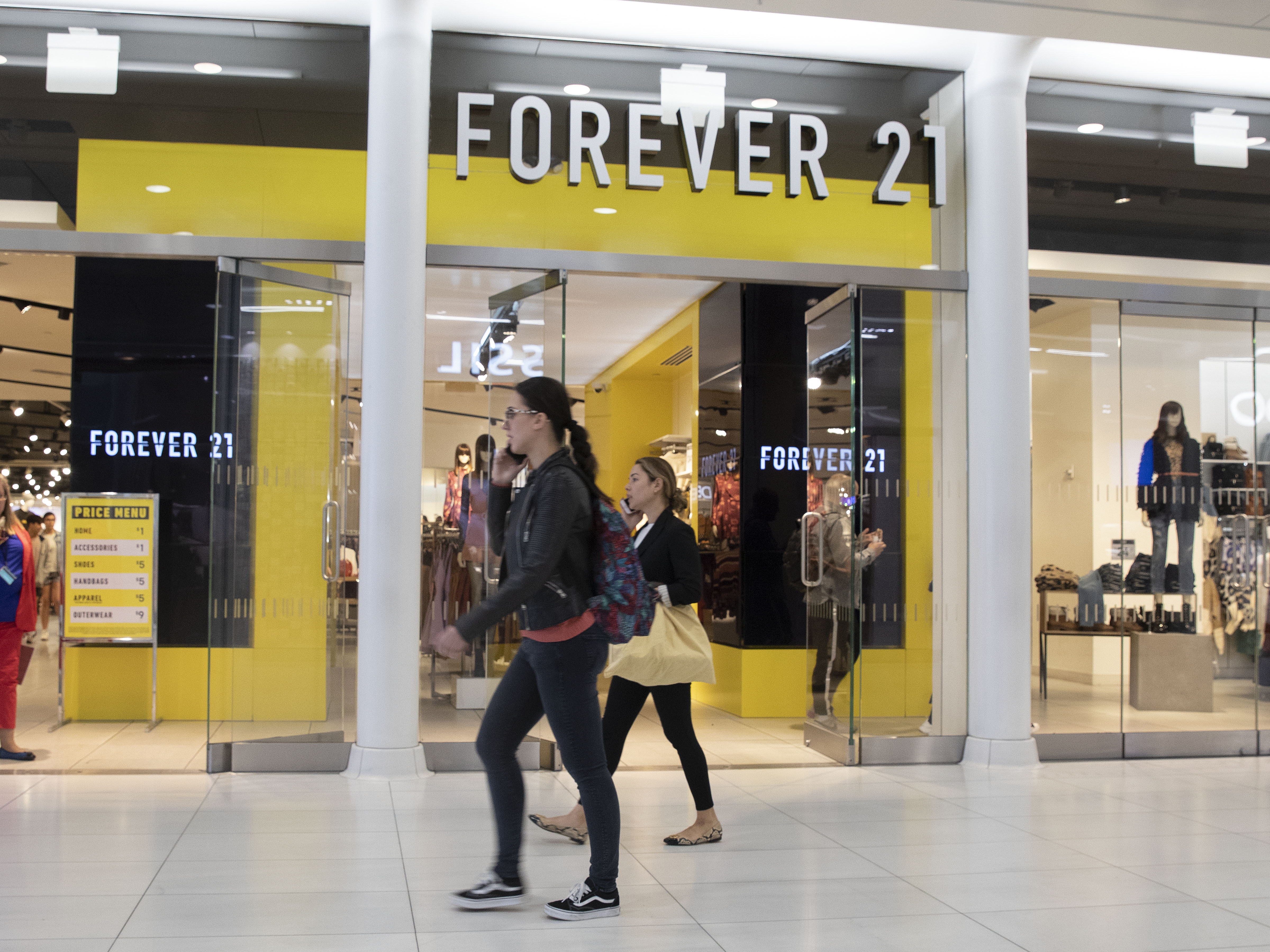 caption: People walk in front of a Forever 21 clothing store in New York.