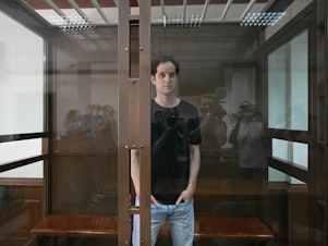 caption: Evan Gershkovich stands inside a defendants' cage before a June hearing in Moscow.