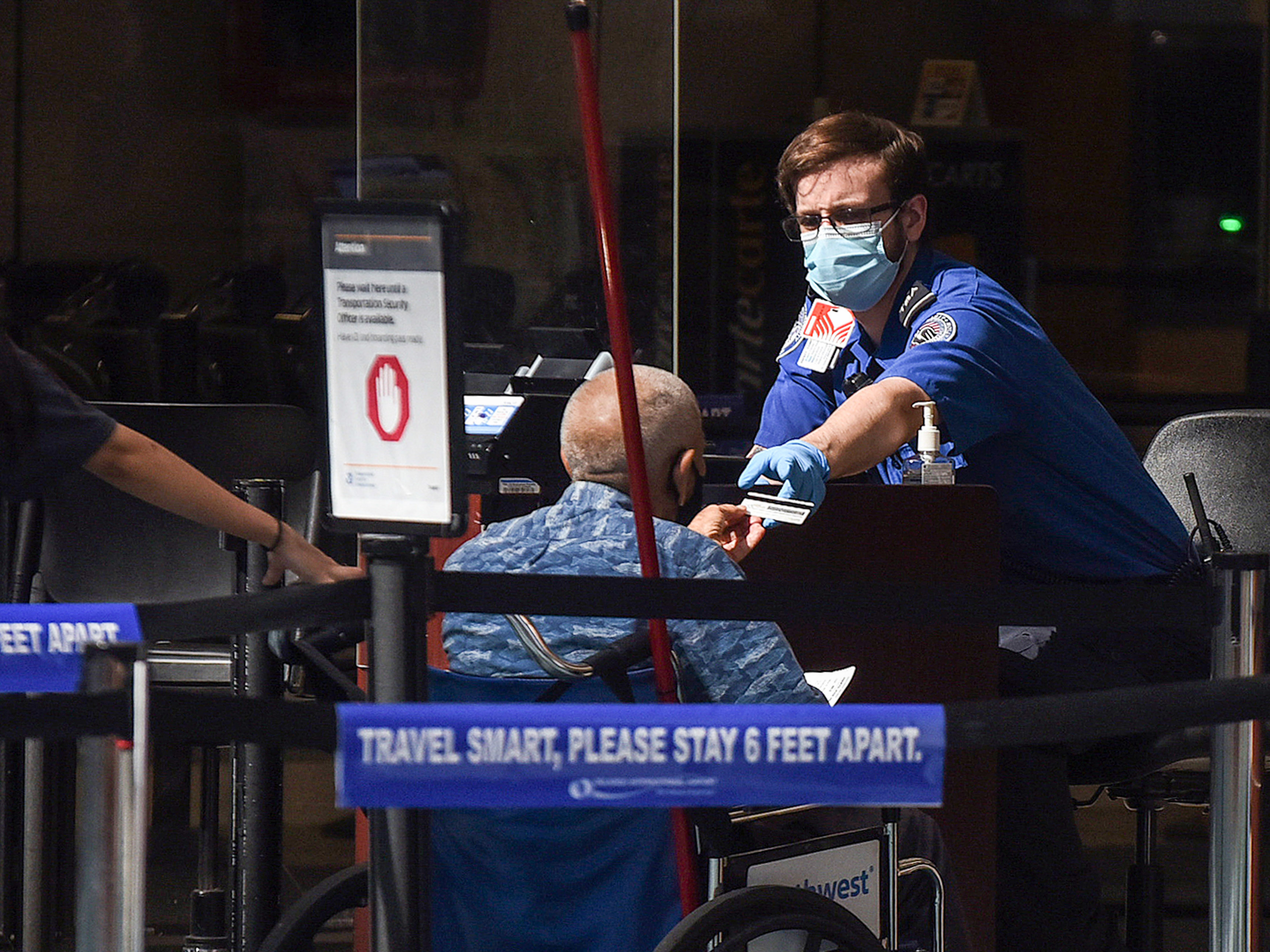caption: A man using a wheelchair hands his ID to an officer at a security screening checkpoint at Orlando International Airport in 2020.