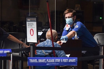 caption: A man using a wheelchair hands his ID to an officer at a security screening checkpoint at Orlando International Airport in 2020.