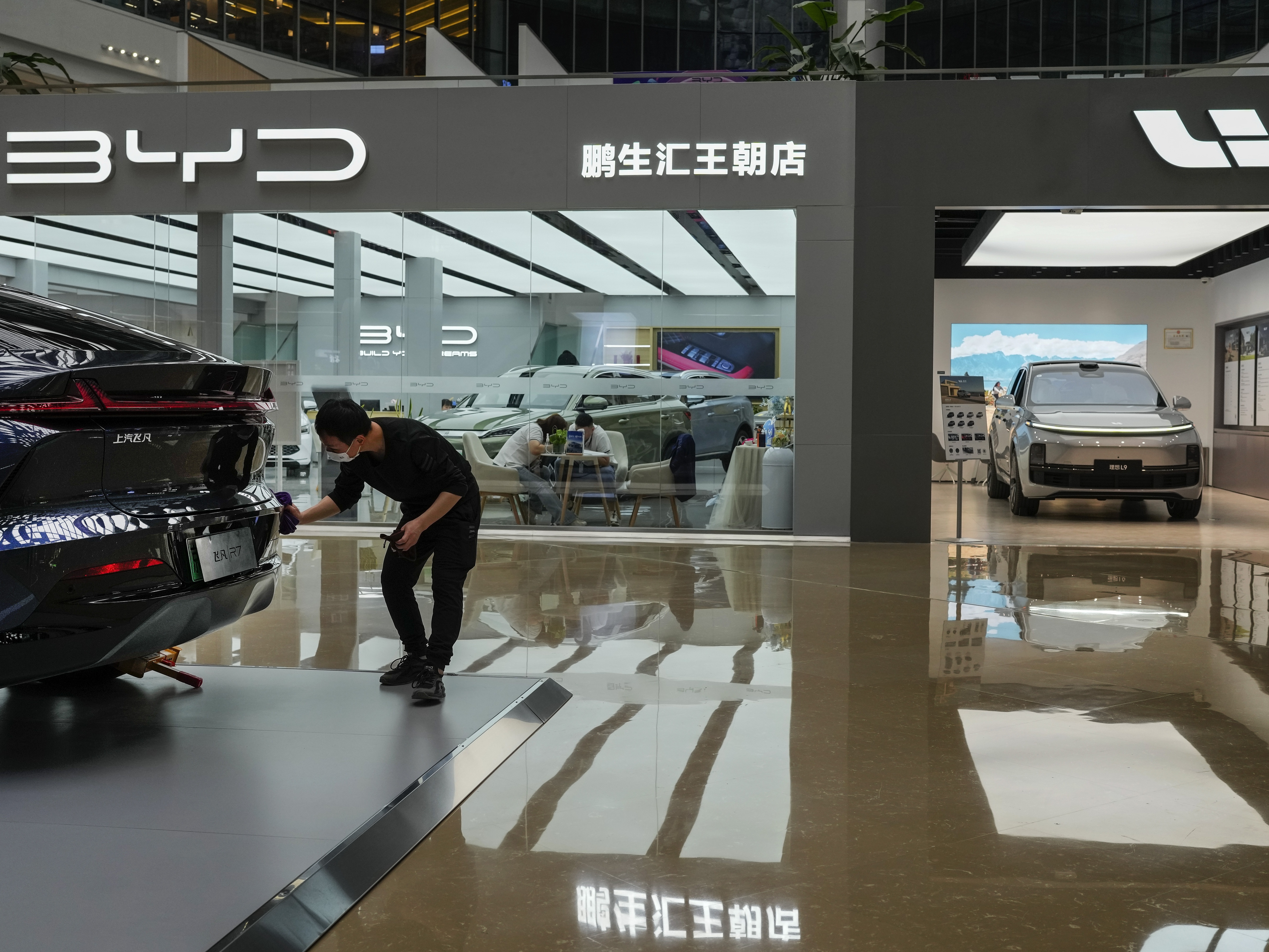 caption: A worker wipes a Rising F7 car model at a floor section selling various Chinese-made electric car brands inside a shopping mall in Beijing, Tuesday, April 4, 2023. (AP Photo/Andy Wong)