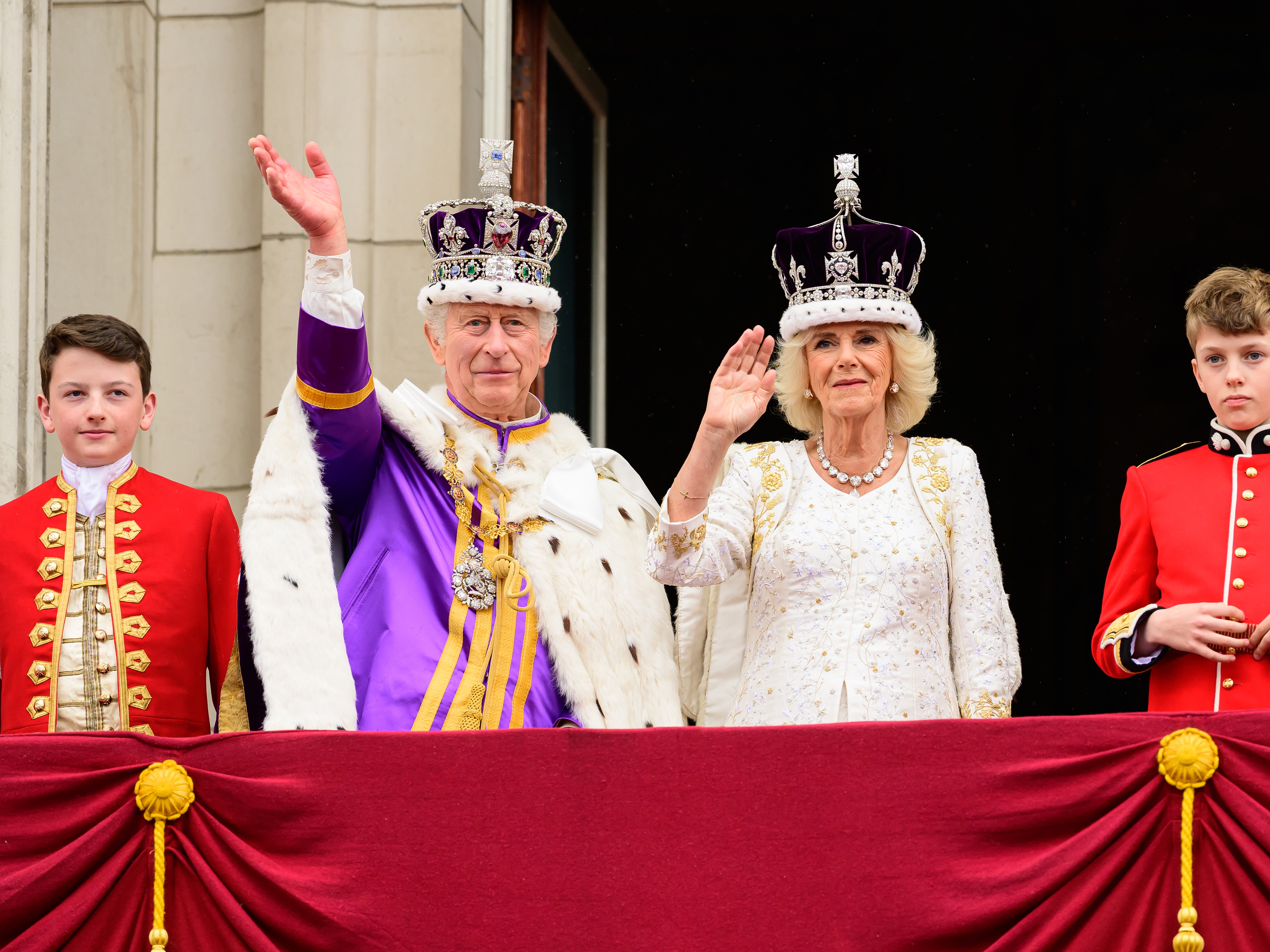 caption: King Charles III and Queen Camilla wave from the balcony of Buckingham Palace during the Coronation of King Charles IIII and Queen Camilla on May 06, 2023 in London, England.