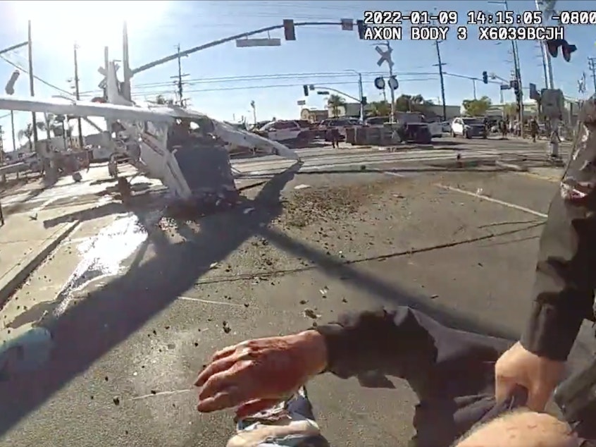 caption: A still image from an LAPD officer's body-worn camera shows the pilot of a small plane being dragged to safety, after his aircraft crash-landed in the path of an oncoming commuter train.