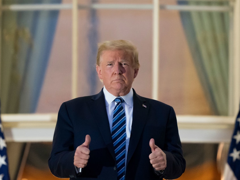 caption: President Donald Trump gives thumbs up as he stands on the Blue Room Balcony upon returning to the White House on Monday.