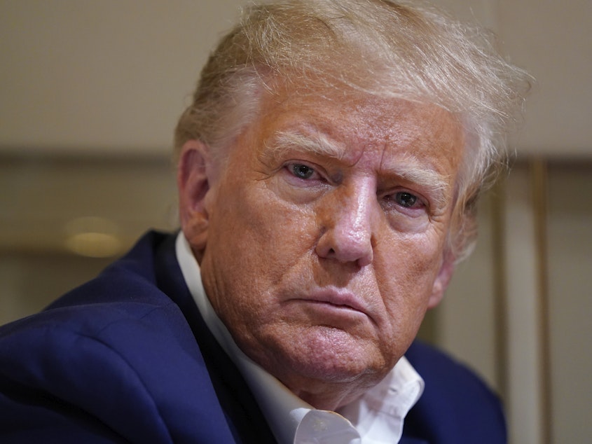 caption: Former President Donald Trump listens as he speaks with reporters while in flight on his plane after a campaign rally in Waco, Texas, on March 25.