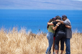 caption: Volunteers helping those who lost homes in Lahaina stop to pray on a hillside. The town is surrounded by dry, invasive grasses which are highly flammable.