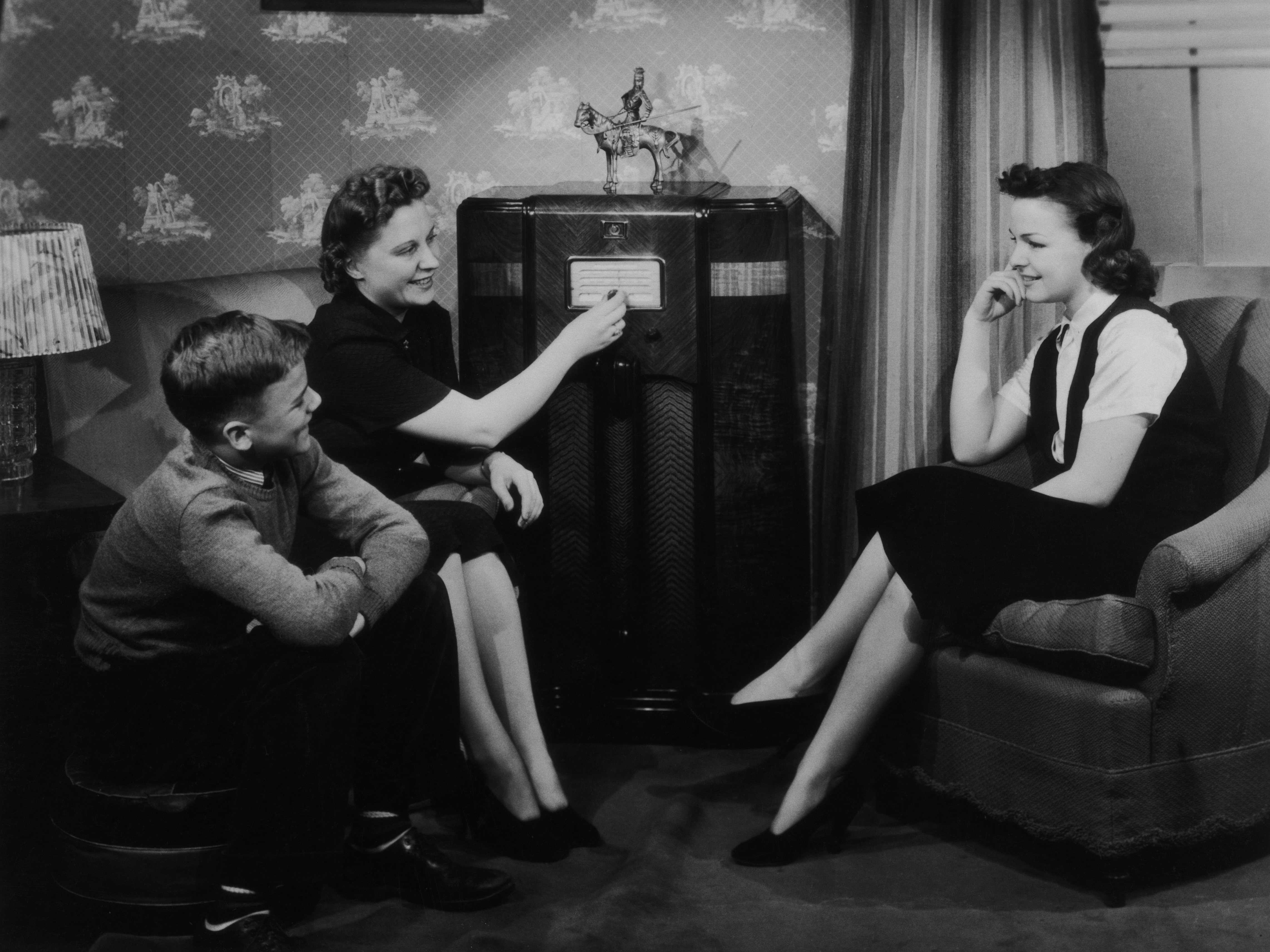 caption: People gather around a large valve radio in 1940. By that point, over 80% of American households owned a radio.