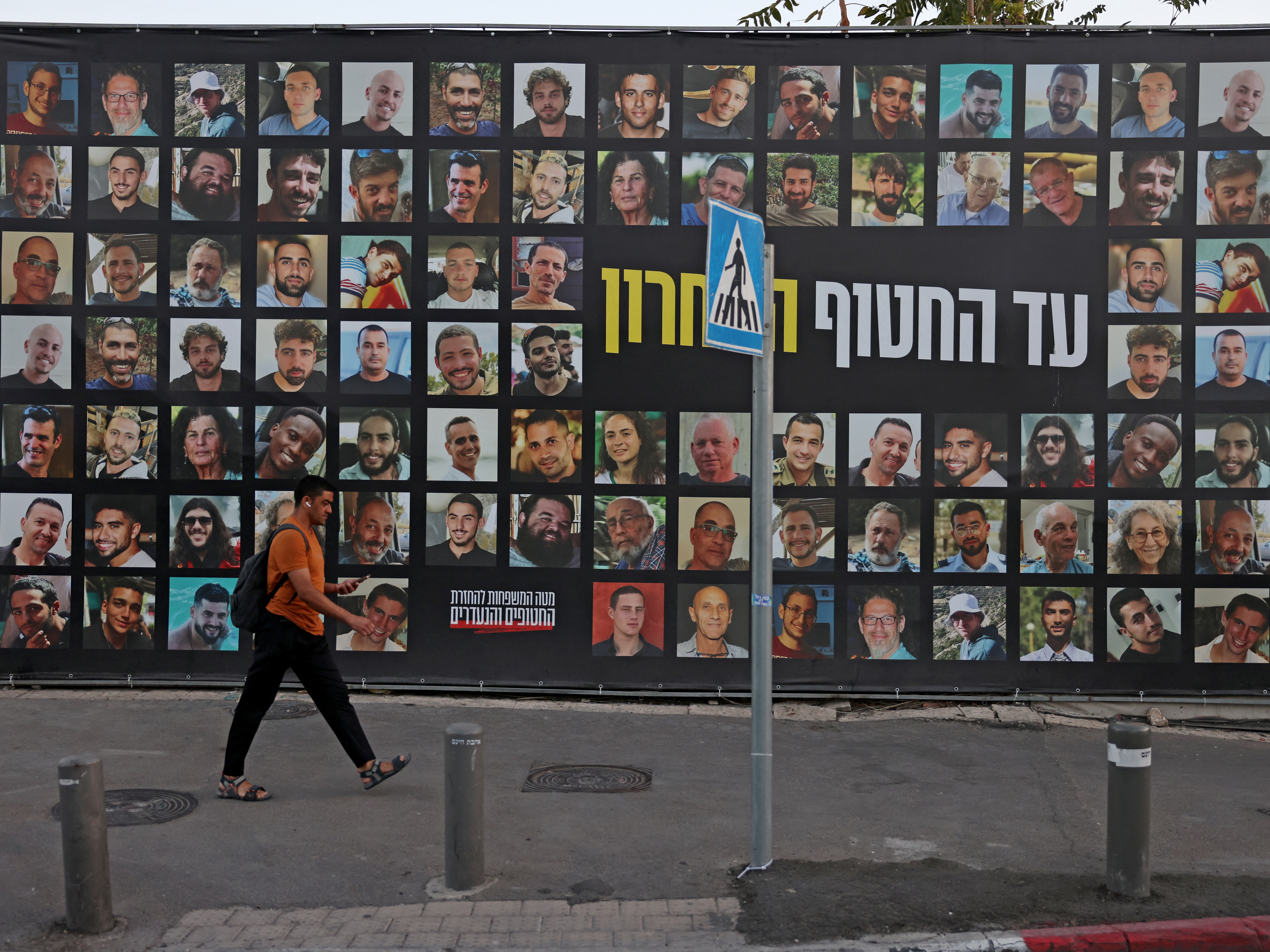 caption: A man walks past a billboard bearing the portraits of Israelis held hostage in the Gaza Strip by Palestinian militants since Oct.2023.