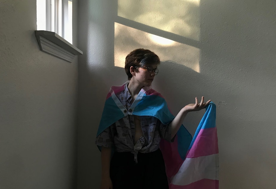 Lazarus Killmer poses with the trans pride flag which consists of five stripes. The two pink and blue stripes represent the traditional gender binary-- pink for girls and blue for boys. The white stripe represents those who are transitioning or those outside the gender binary.