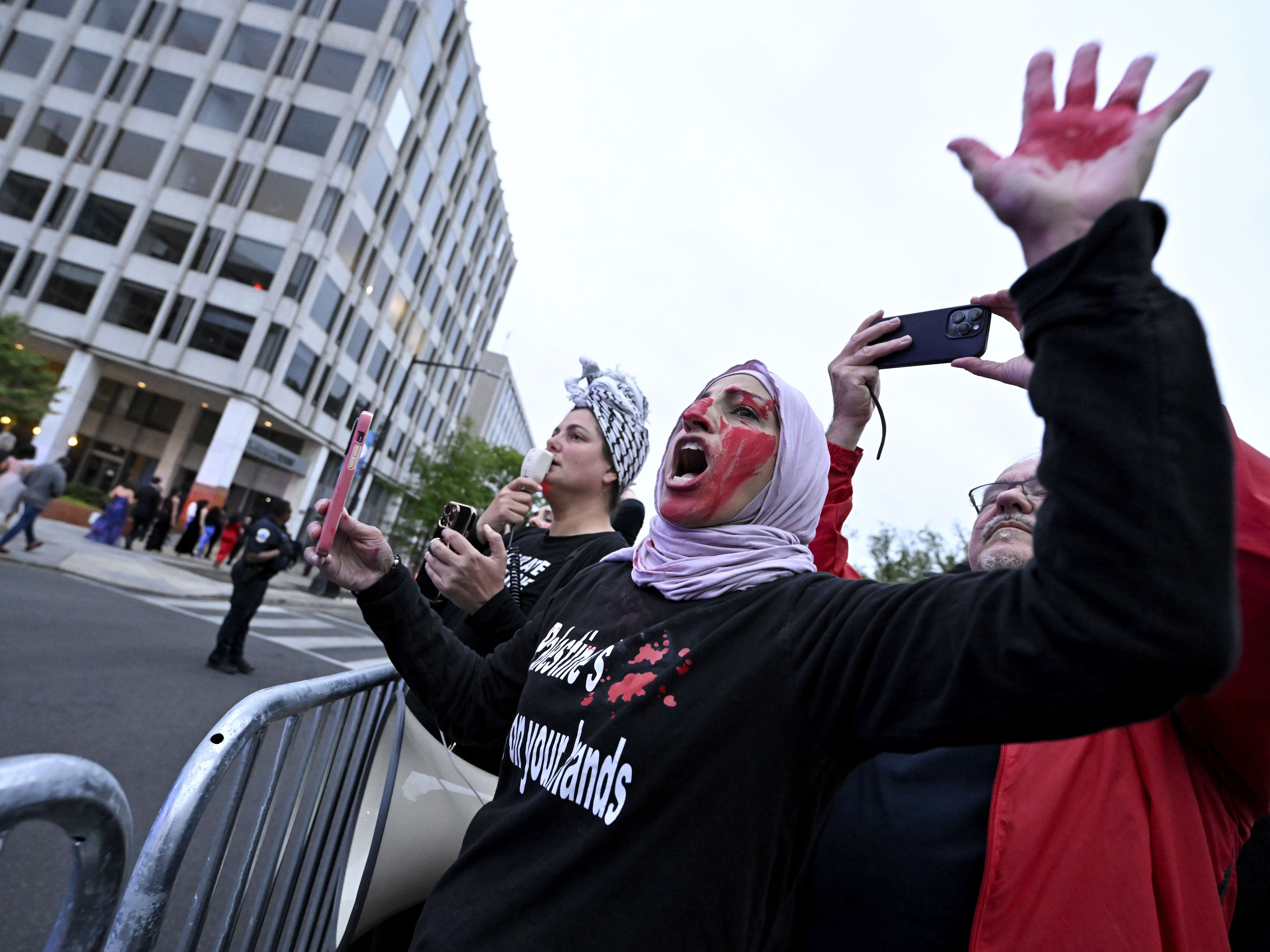 caption: A demonstrator with red paint on their hand and face is seen behind a police barricade during a pro-Palestinian protest over the Israel-Hamas war at the White House Correspondents' Association Dinner, Saturday April 27, 2024, in Washington.