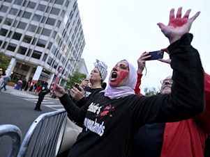 caption: A demonstrator with red paint on their hand and face is seen behind a police barricade during a pro-Palestinian protest over the Israel-Hamas war at the White House Correspondents' Association Dinner, Saturday April 27, 2024, in Washington.