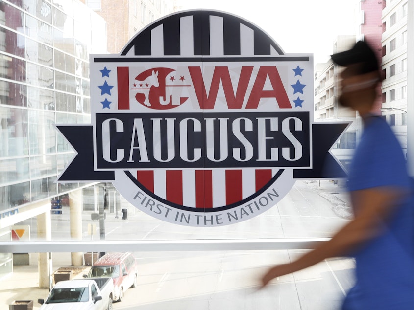 caption: A pedestrian walks past a sign for the Iowa caucuses on a downtown skywalk in Des Moines, Iowa, on Feb. 4, 2020.