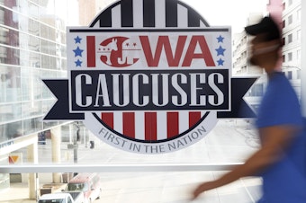 caption: A pedestrian walks past a sign for the Iowa caucuses on a downtown skywalk in Des Moines, Iowa, on Feb. 4, 2020.