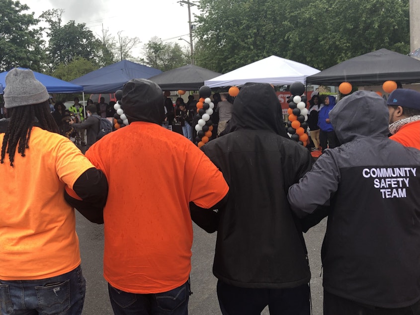 caption: People stand in the rain and link arms at an event for National Gun Violence Awareness Day in Skyway, Washington on June 3, 2022.