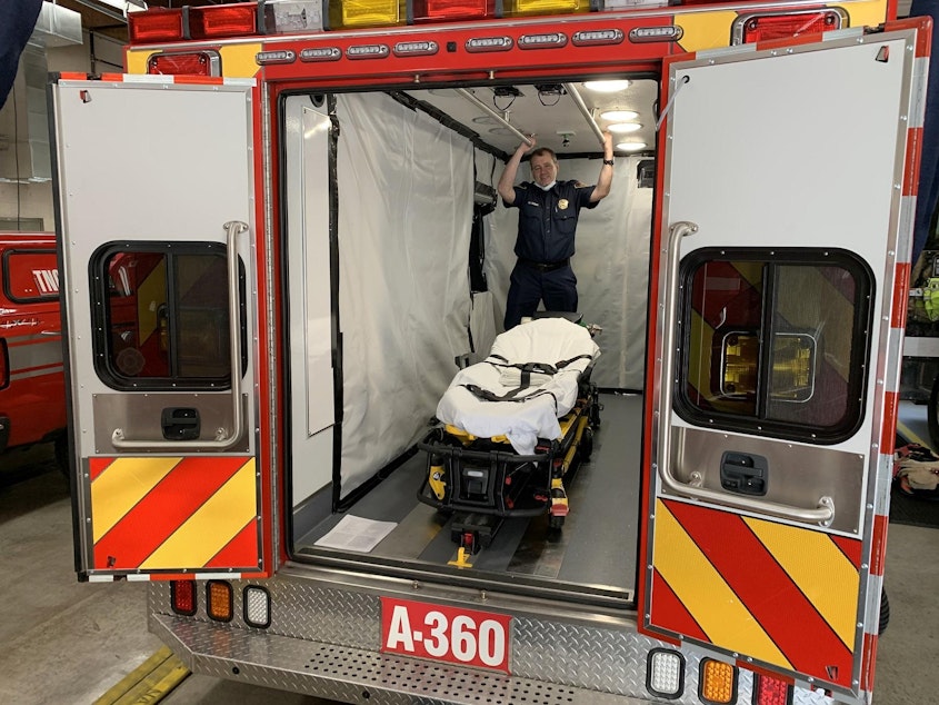 caption: South King Fire and Rescue Lt. Greg Willett stands in an aid car optimized to transport COVID-positive patients.