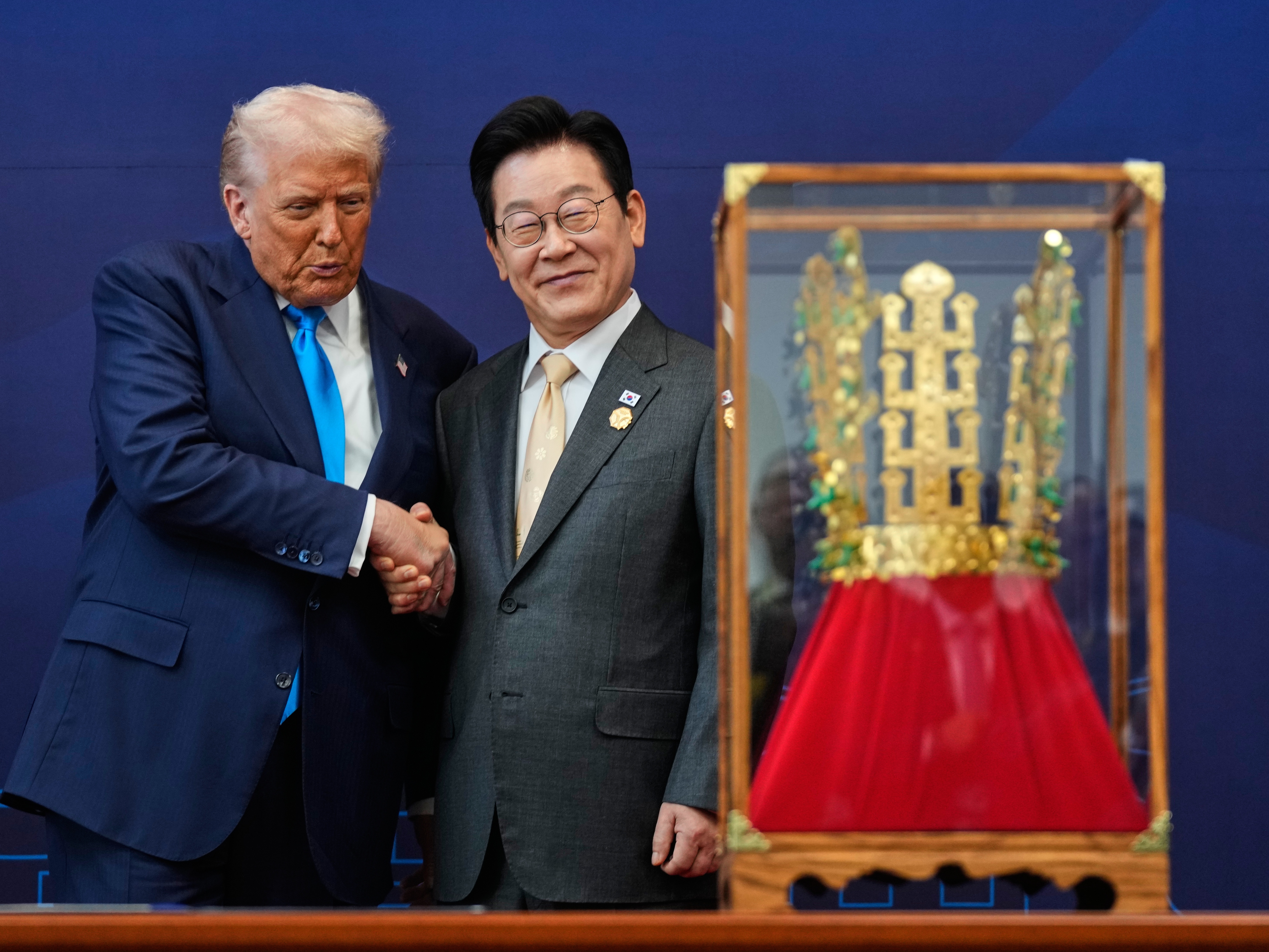 caption: President Trump shakes hands with South Korean President Lee Jae Myung as he receives a gift of a gold crown and an award of the Grand Order of Mugunghwa, not seen, during a high honor ceremony at the Gyeongju National Museum in Gyeongju, South Korea, on Wednesday.