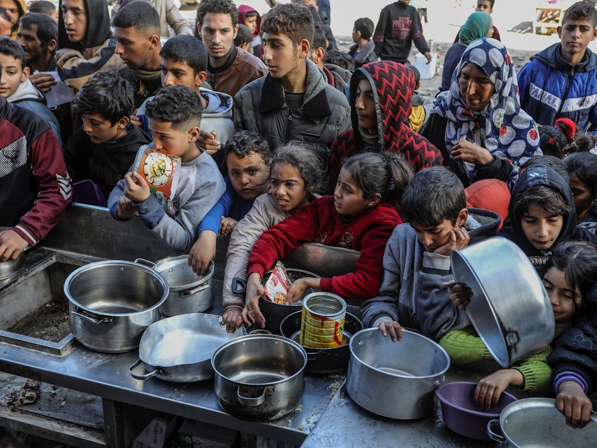 caption: Palestinian people with empty bowls wait for food at a donation point in Rafah. A report out this week shows widespread hunger and malnutrition in Gaza but stopped short of declaring it a "famine."