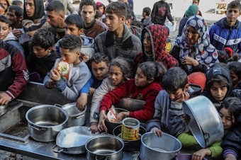 caption: Palestinian people with empty bowls wait for food at a donation point in Rafah. A report out this week shows widespread hunger and malnutrition in Gaza but stopped short of declaring it a "famine."