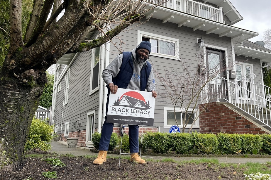 caption: Chukundi Salisbury places a new sign in front of a home owned by a member of the Black Legacy Homeowners' group in Seattle's Central District.