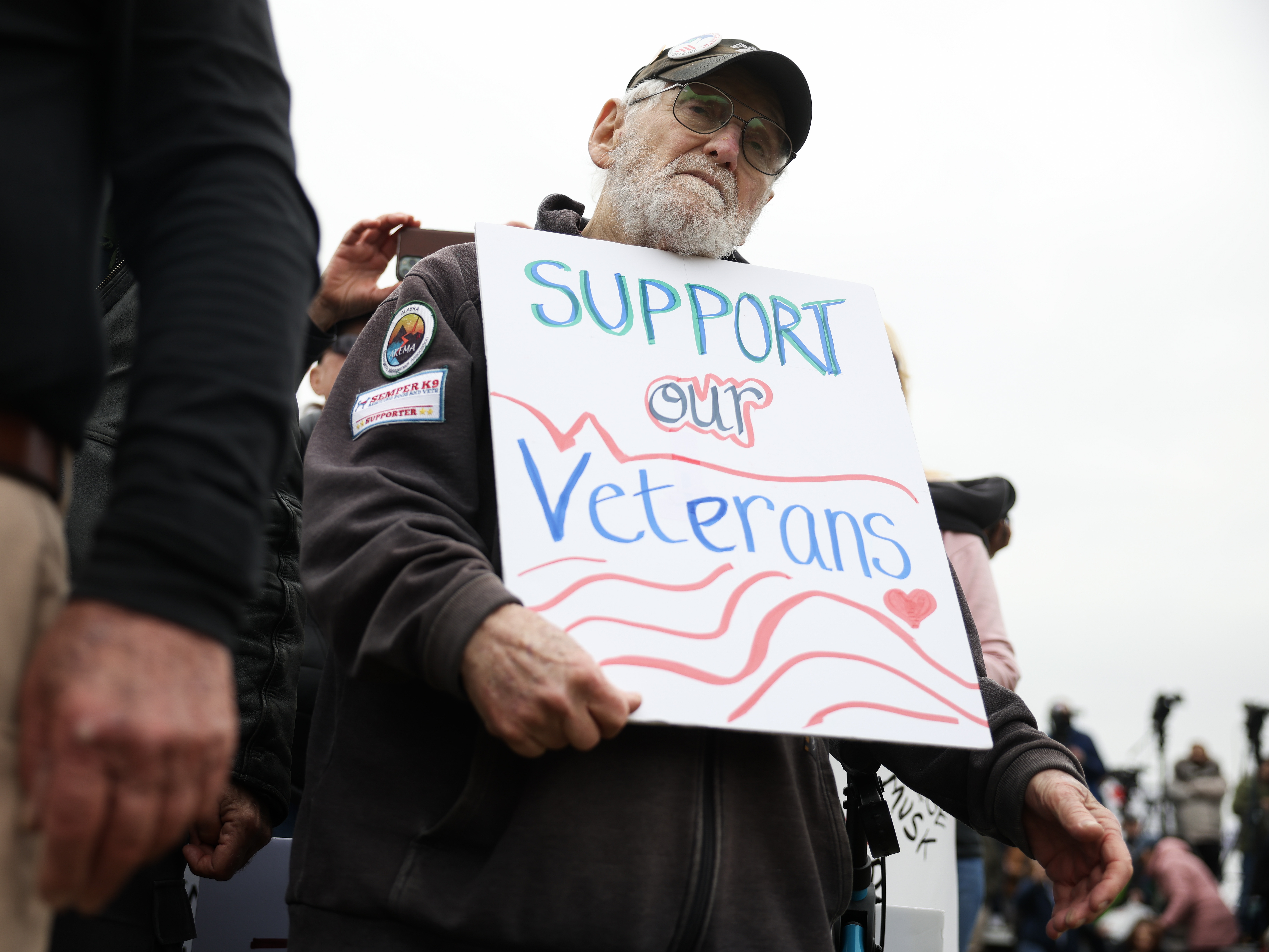 caption: John Spitzberg, 87, holds a "Support our Veterans" sign during a veterans march at the National Mall on March 14 in Washington, D.C. The 87-year-old veteran was arrested June 13 at the U.S. Capitol while protesting the U.S. Army's 250th anniversary parade, which coincided with President Trump's 79th birthday.