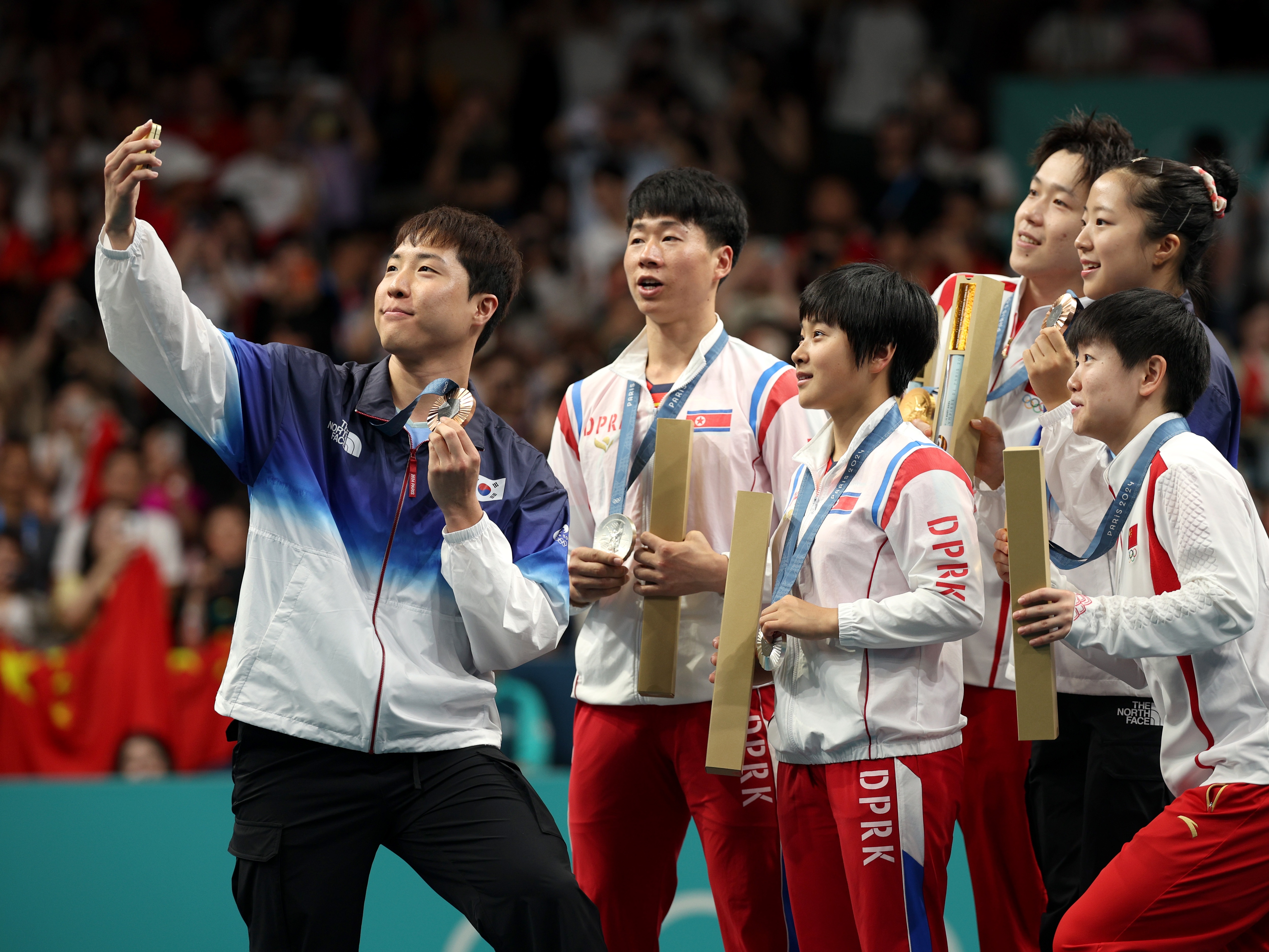 caption: Lim Jong-hoon of South Korea takes a selfie with North Korean silver medalists Kim Kum-yong and Ri Jong-sik, center, with Chinese gold medalists Wang Chuqin and Sun Yingsha flanking South Korean Shin Yu-bin.