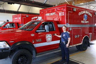 caption: Ocean Shores firefighter/EMT Kara McDermott spends more time than usual behind to wheel of these ambulances as overwhelmed hospitals routinely divert incoming transports.