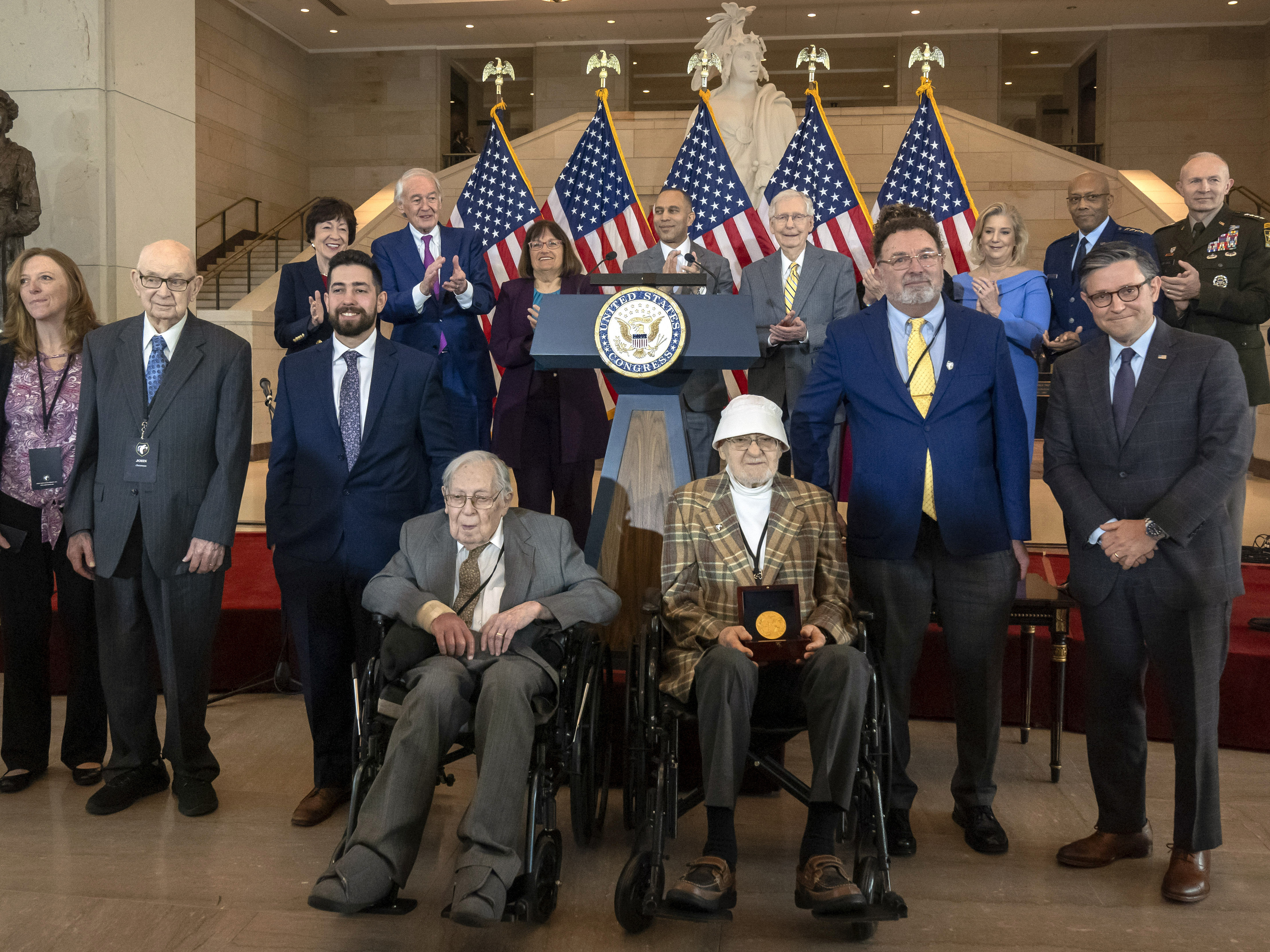 caption: Ghost Army members John Christman, of Leesburg, N.J., second from left standing, Seymour Nussenbaum, of Monroe Township, N.J, in wheelchair at left, and Bernard Bluestein, of Hoffman Estates, Ill., in wheelchair at right, join military and congressional officials as members of their secretive WWII-era unit are presented with the Congressional Gold Medal on Thursday.