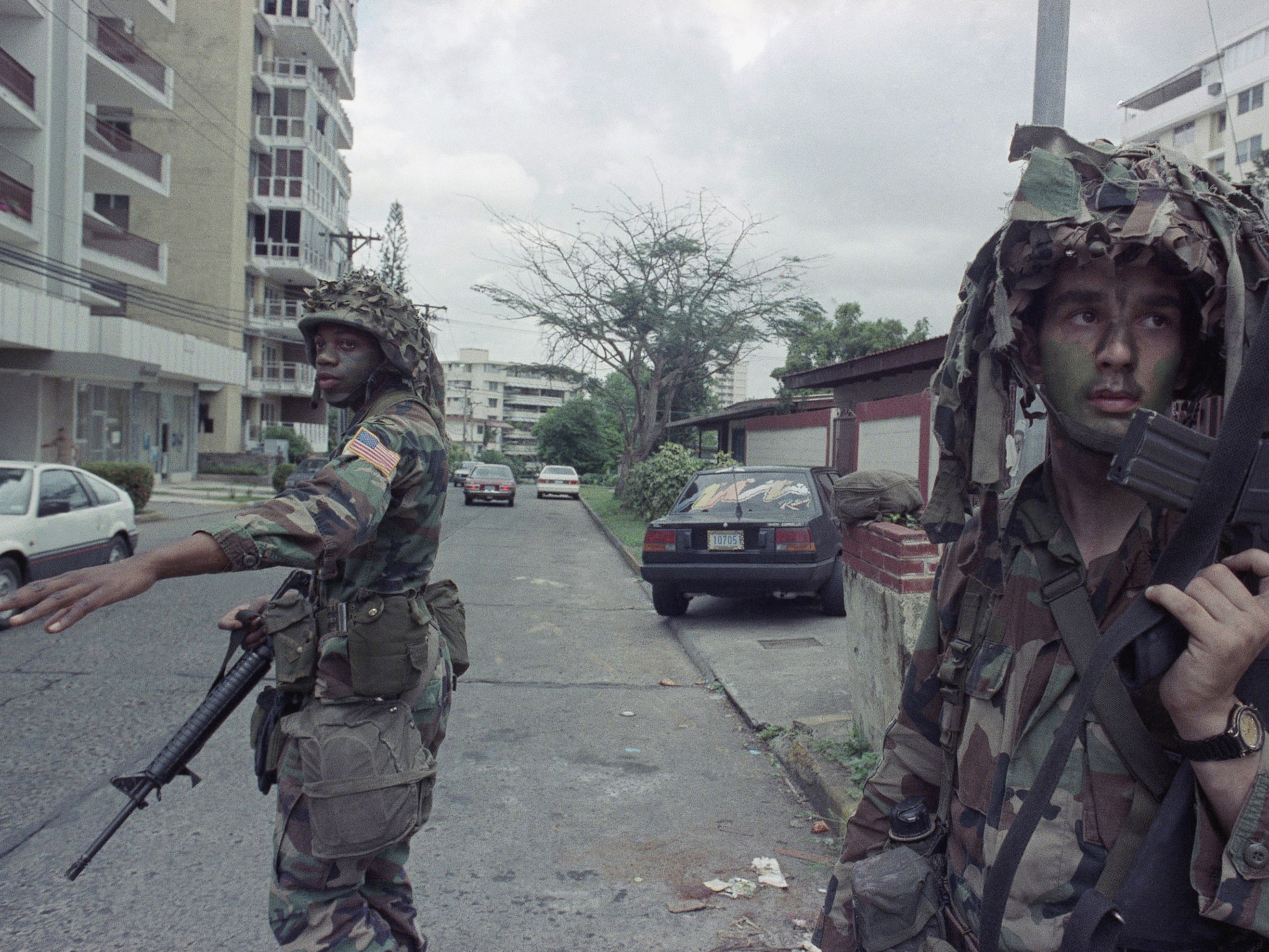 caption: U.S. soldiers direct traffic outside the residence of the Peruvian ambassador to Panama, right rear, in Panama City on Jan. 9, 1990. In December 1989, U.S. President George H.W. Bush sent thousands of troops to Panama to arrest the country's leader, Manuel Noriega.