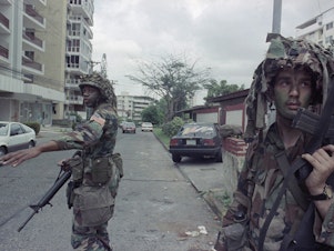 caption: U.S. soldiers direct traffic outside the residence of the Peruvian ambassador to Panama, right rear, in Panama City on Jan. 9, 1990. In December 1989, U.S. President George H.W. Bush sent thousands of troops to Panama to arrest the country's leader, Manuel Noriega.