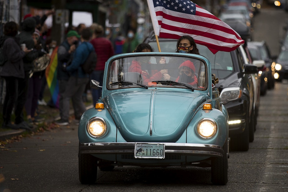 caption: Joshua Trujillo drives as his daughters, Ravenna, 14, and Araya, 12, wave an American flag to celebrate the first female Vice President in America during an impromptu car parade and celebration after the results of the 2020 presidential election were made official on Saturday, November 7, 2020, near the intersection of 10th Avenue and East Pine Street in Seattle.