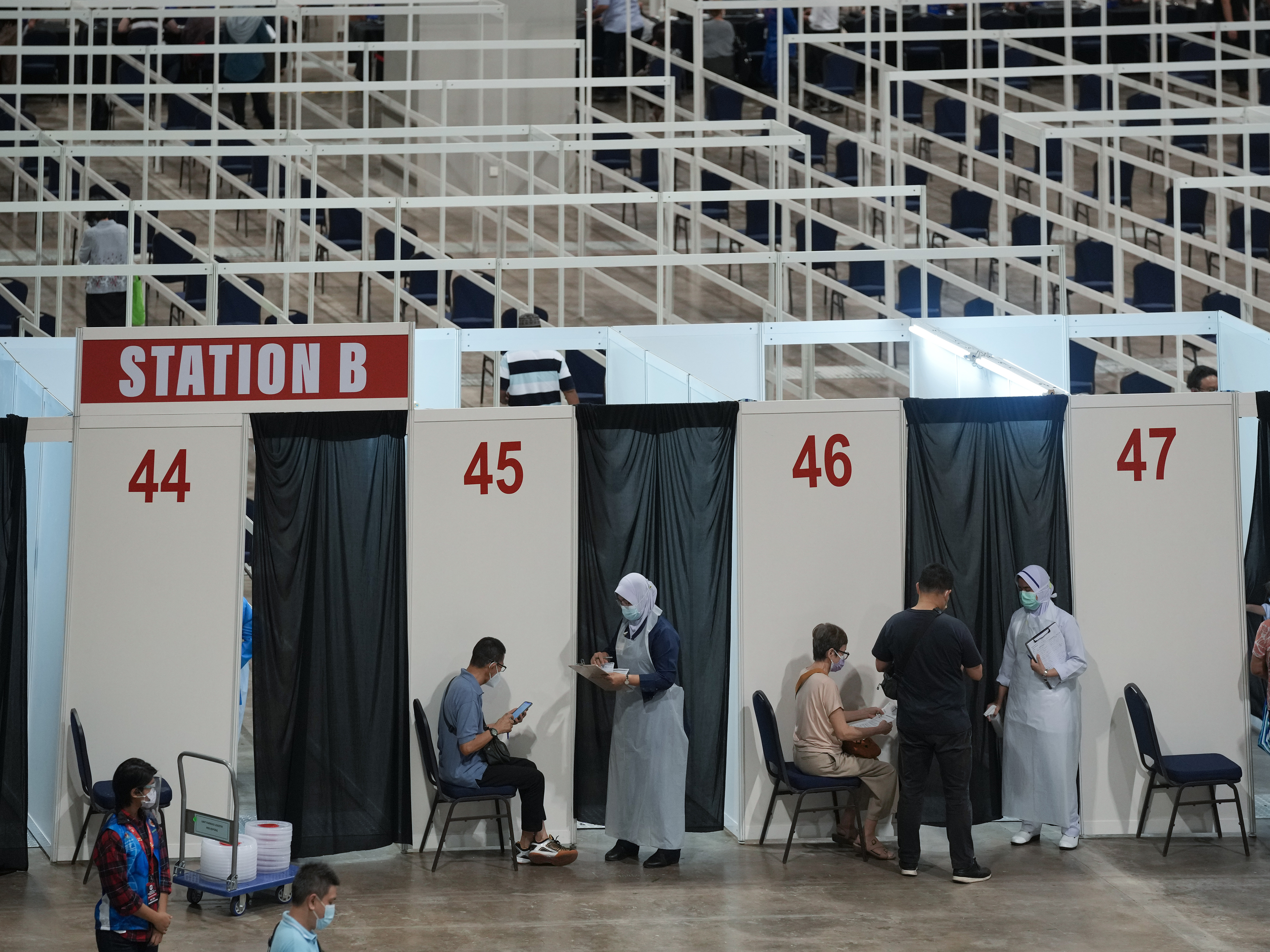 caption: Health staff and patients at an exhibition center in Kuala Lumpur that's been turned into Malaysia's first mega-vaccination center. The government aims to speed up inoculations amid a sharp spike in infections.