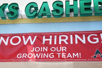 caption: A 'Now Hiring' sign is displayed outside a check cashing shop in Los Angeles on June 2, 2023. Employers added 209,000 jobs last month, slowing down from previous months but still marking respectable growth.