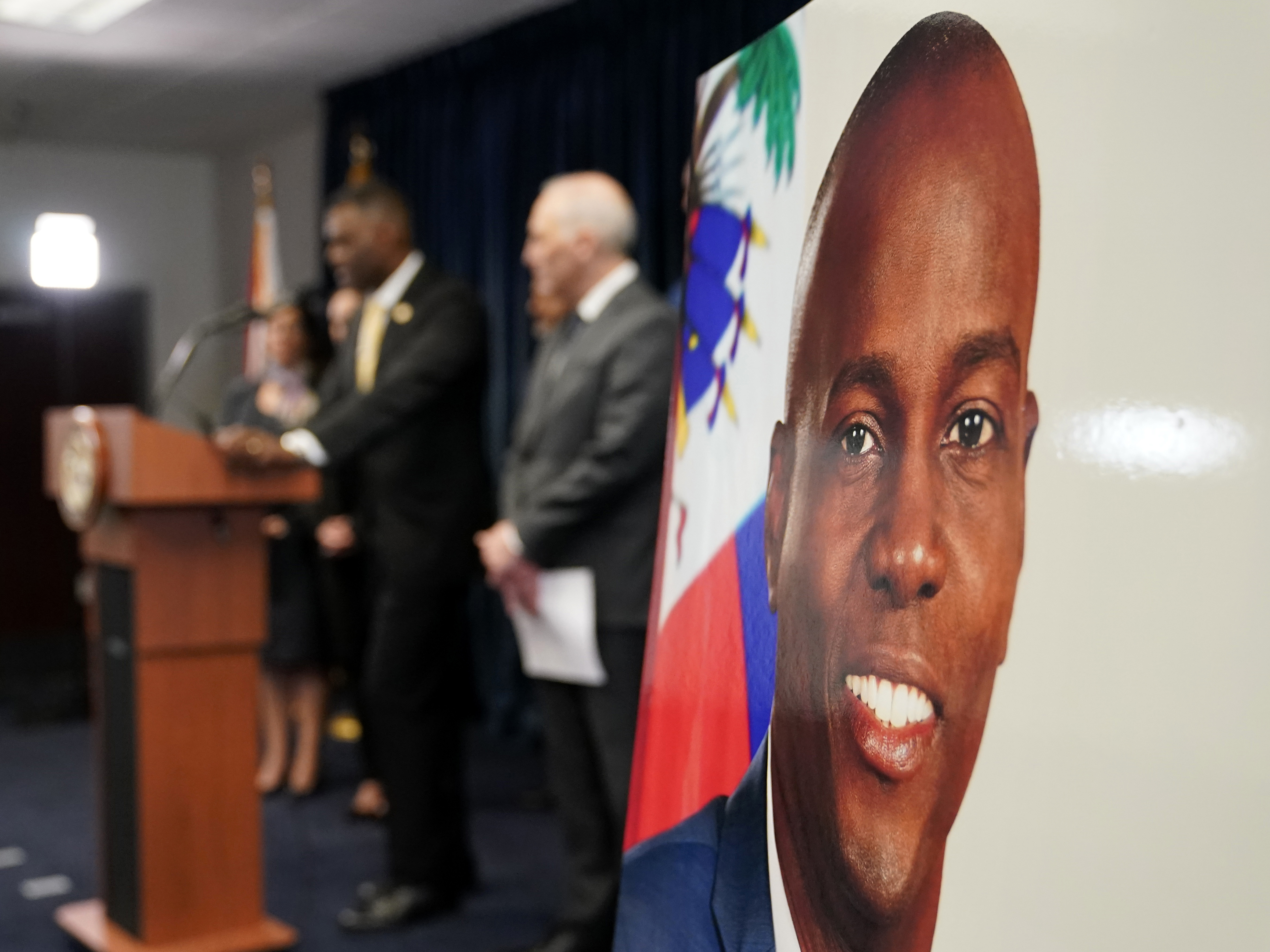 caption: An image of Haitian President Jovenel Moïse, right, is displayed as Markenzy Lapointe, U.S. Attorney for the Southern District of Florida, speaks speaks during a news conference, Tuesday, Feb. 14, 2023, in Miami.