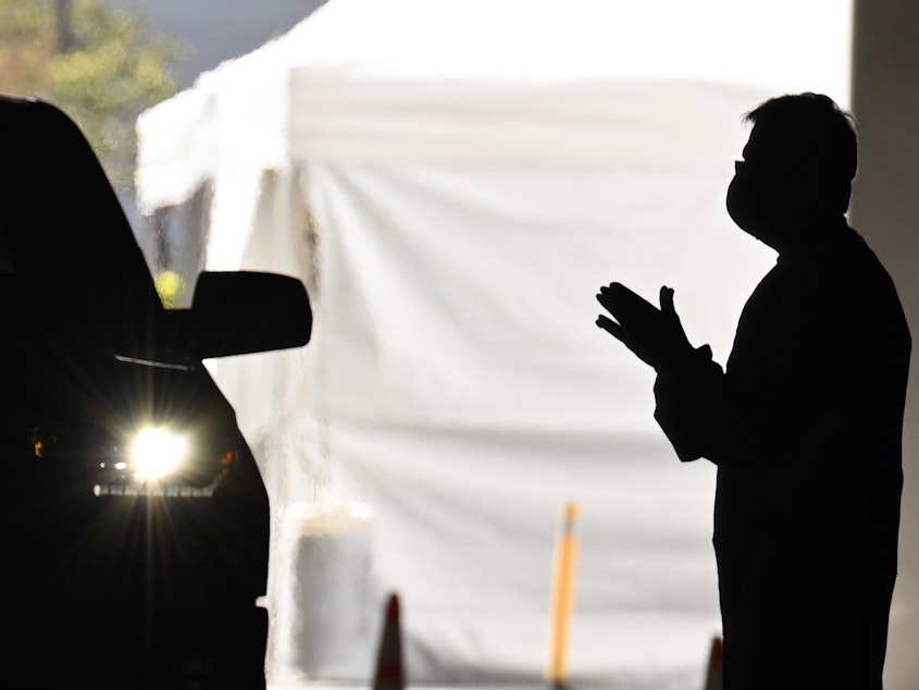 caption: A health care worker instructs people arriving in their cars to be tested for COVID-19 at a new coronavirus drive through testing site in Redondo Beach, Calif.