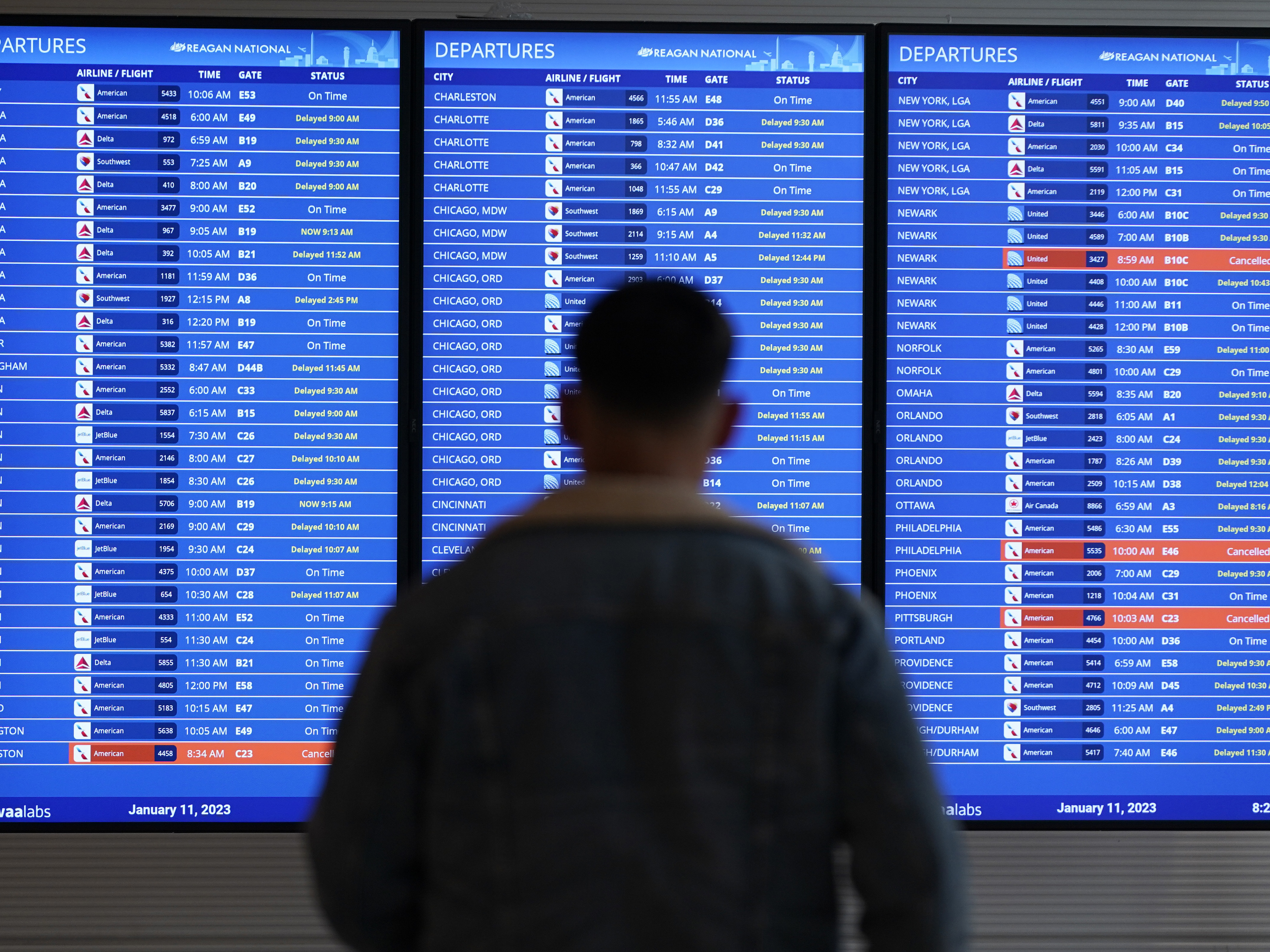 caption: A traveler looks at a flight board with delays and cancellations at Ronald Reagan Washington National Airport in Arlington, Va., on Jan. 11, 2023.