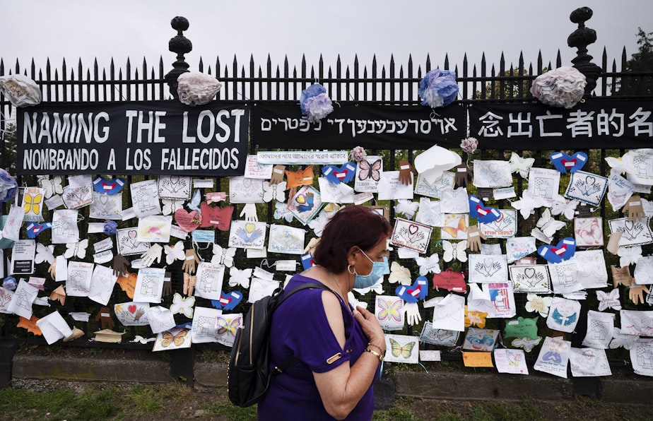 caption: In this May 28, 2020, file photo, a woman passes a fence outside Brooklyn's Green-Wood Cemetery adorned with tributes to victims of COVID-19 in New York. The U.S. death toll from the coronavirus topped 200,000 Tuesday, Sept. 22, a figure unimaginable eight months ago when the scourge first reached the world’s richest nation with its sparkling laboratories, top-flight scientists and towering stockpiles of medicines and emergency supplies. (Mark Lennihan/AP Photo File)