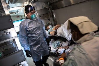 caption: An EMT wearing personal protective equipment prepares to unload COVID-19 transfer patients in the early days of the pandemic. The Biden Administration has just announced a new program aimed at preventing the next pandemic.