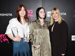 caption: Billie Eilish at the 32nd Environmental Media Association (EMA) Awards Gala in Los Angeles, Oct. 8 2022. The pop star is flanked by her mother Maggie Baird (left) and EMA CEO Debbie Levin.