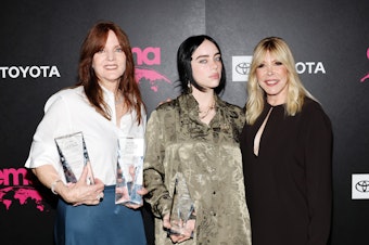 caption: Billie Eilish at the 32nd Environmental Media Association (EMA) Awards Gala in Los Angeles, Oct. 8 2022. The pop star is flanked by her mother Maggie Baird (left) and EMA CEO Debbie Levin.
