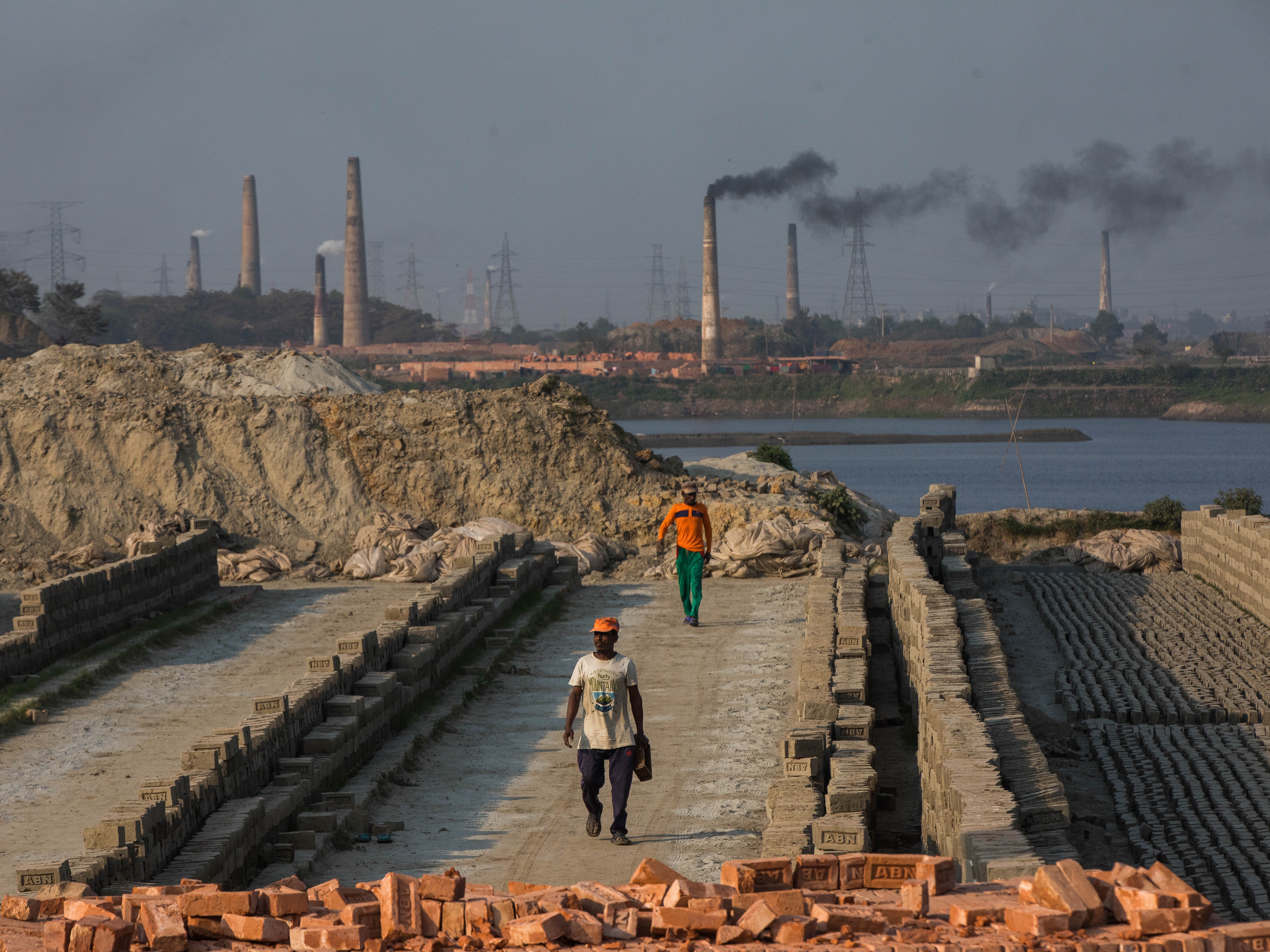 caption: Smoke comes out from kilns at a brickfield on the outskirt of Dhaka, Bangladesh on February 6, 2021.