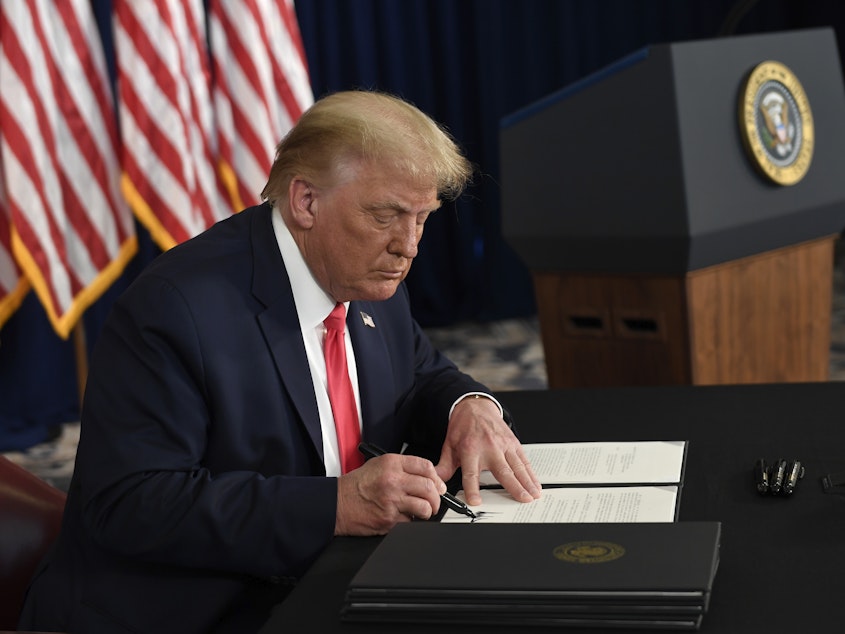 caption: President Trump signs one of four executive orders addressing the economic fallout from the pandemic in Bedminster, N.J., on Aug. 8. The Trump administration has given employers the option to stop collecting payroll taxes, but workers may have to repay the money next year.
