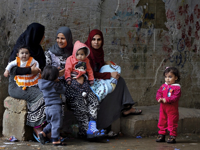 caption: Syrian refugee women hold their children in a refugee compound in the southern port city of Sidon, Lebanon.