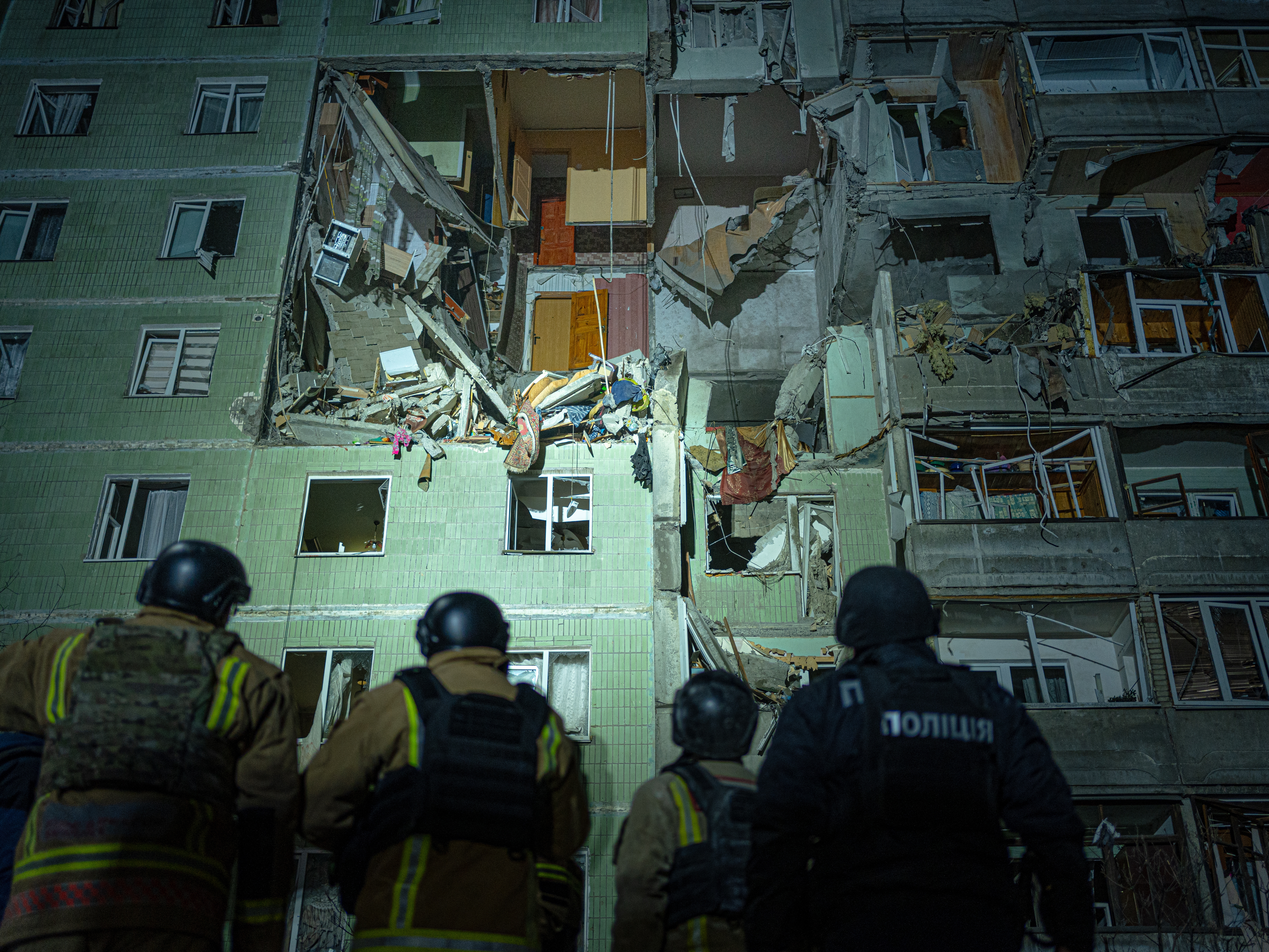 caption: A rescue team gathers in front of a damaged residential building in Sumy just after a Russian drone strike that destroyed nine apartments and killed 11 people, Jan. 30.