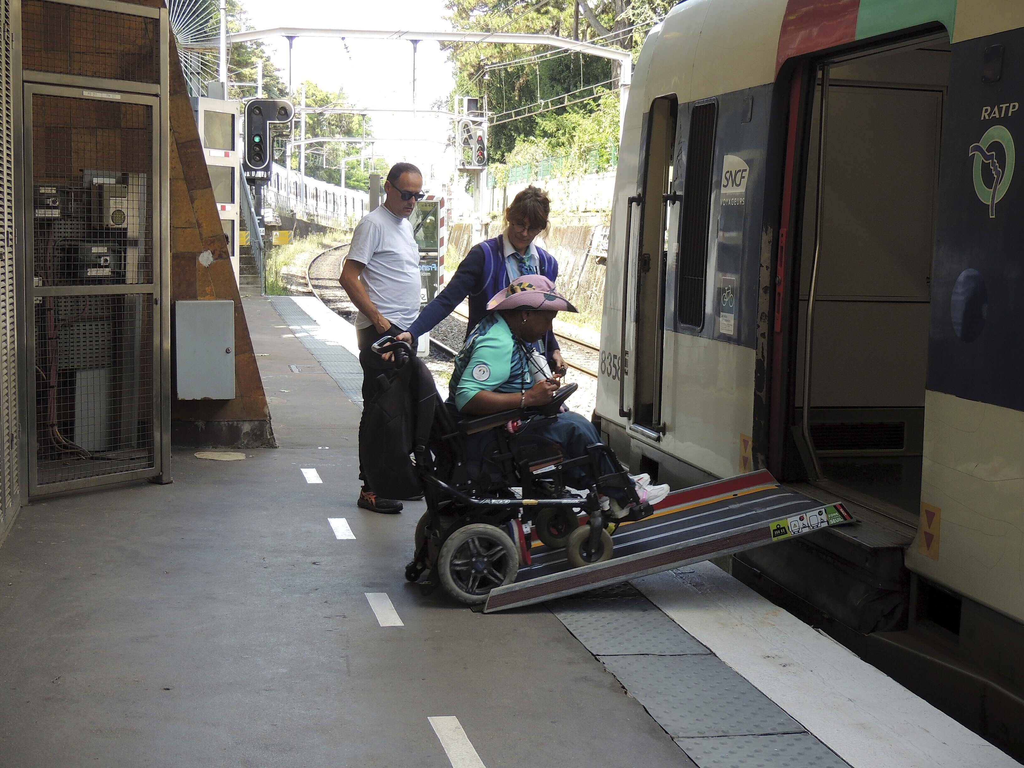 caption: Ndieme Lame, a 57-year-old volunteer for the Paris 2024 Olympic and Paralympic Games navigates a ramp to join a RER train with the help of rail agents, during the 2024 Summer Olympics, on Wednesday in Paris, France. 
