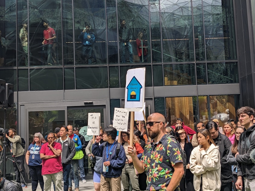 caption: Some Amazon employees walk out in protest while others watch from an office tower above.