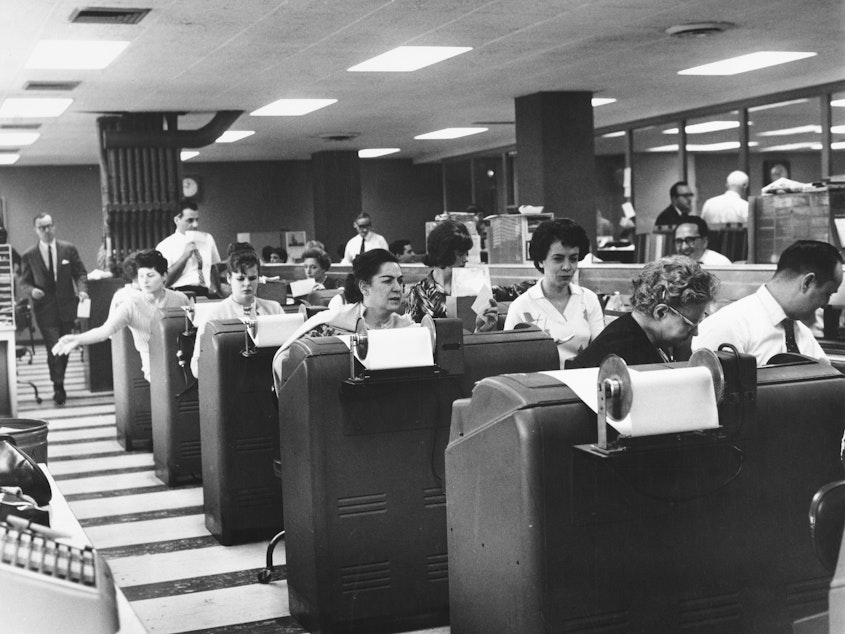 caption: Employees of Goodbody & Co. work at the stock brokerage's headquarters in Manhattan, N.Y., circa 1965.