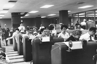 caption: Employees of Goodbody & Co. work at the stock brokerage's headquarters in Manhattan, N.Y., circa 1965.