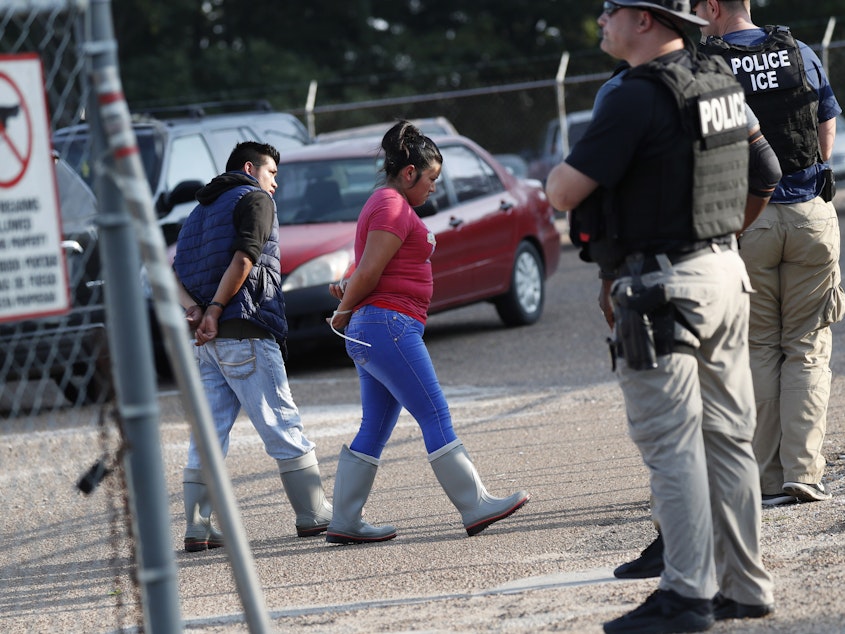 caption: Two people are taken into custody by ICE agents at a Koch Foods Inc. plant in Morton, Miss., one of seven food processing plants targeted for coordinated raids in the state.