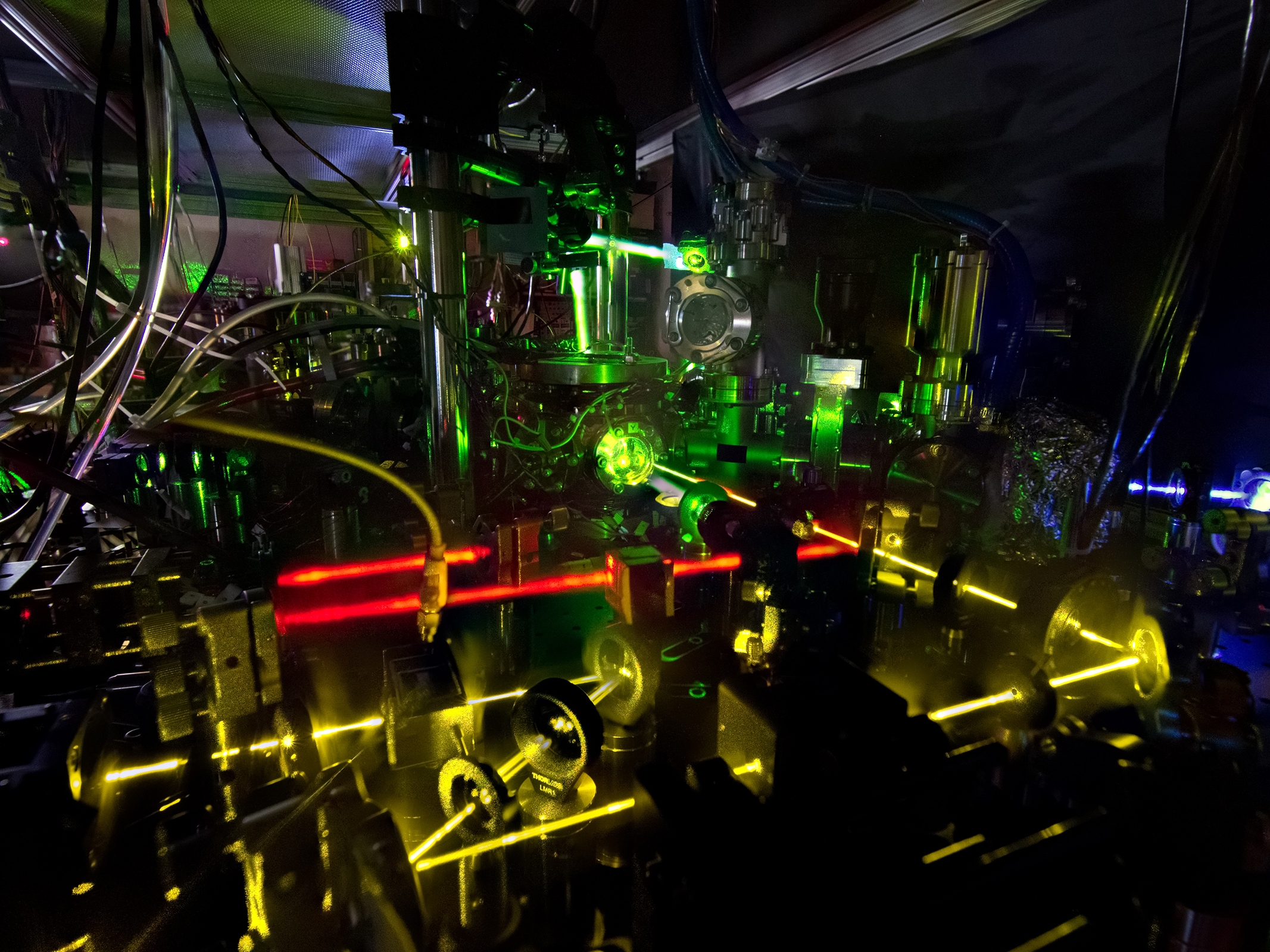 caption: Lasers shine as part of an advanced atomic clock at NIST. Precise measurements of the colors of light emitted by atoms are essential to everything from atomic clocks to medical devices.
