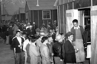 caption: People of Japanese descent wait in line for their assigned homes at an internment camp reception center in Manzanar, Calif., the same camp in which John Tateishi was detained as a child.